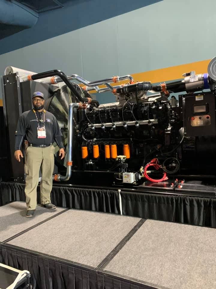 A man is standing on a stage in front of a large engine.