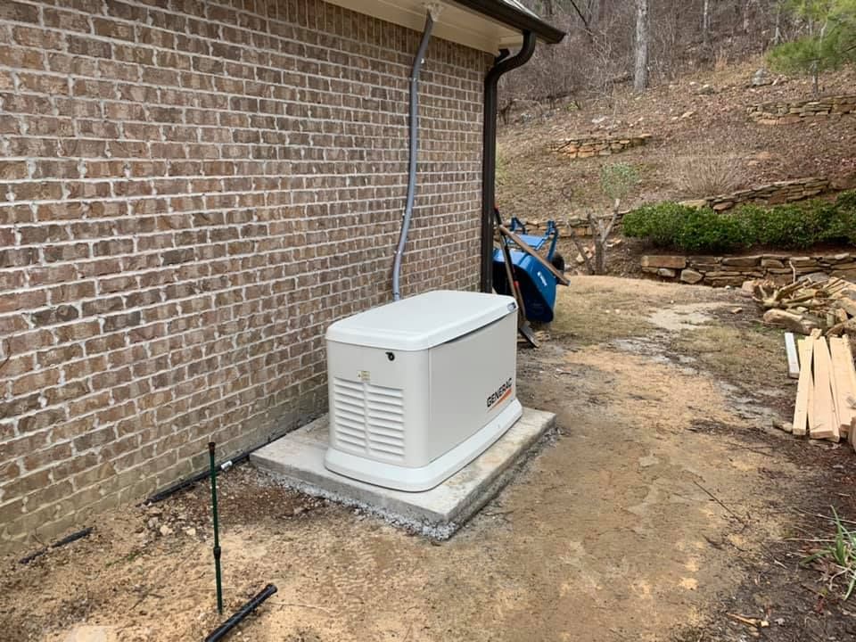 A generator is sitting on the side of a brick building.