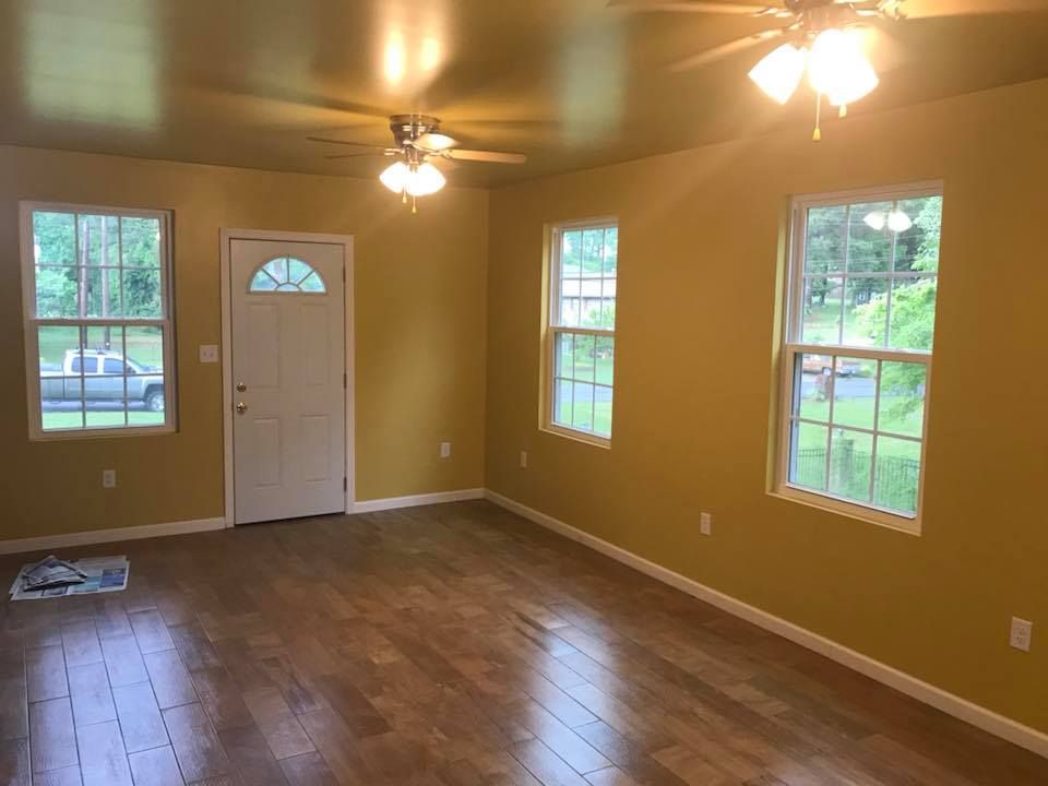 An empty living room with hardwood floors , yellow walls and a ceiling fan.