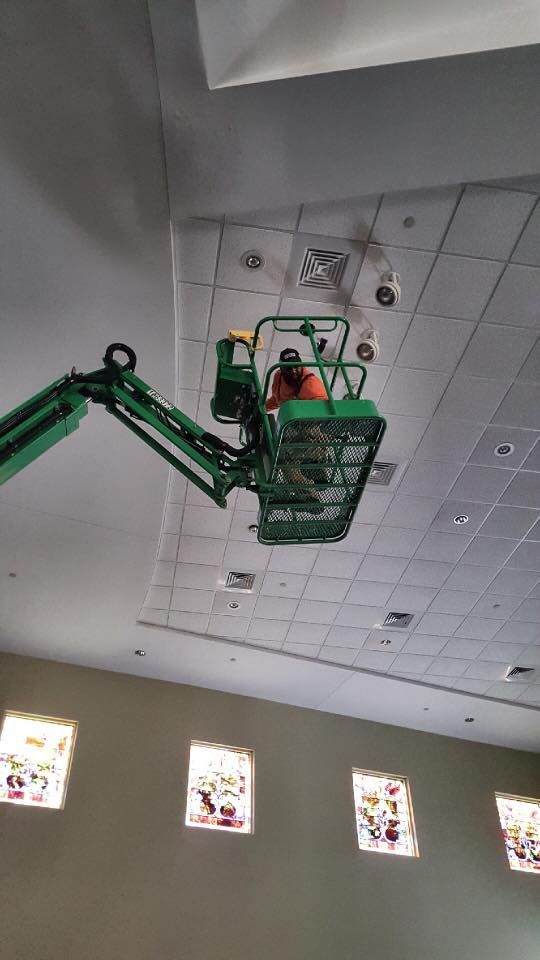 A man is sitting on a lift working on the ceiling of a building.