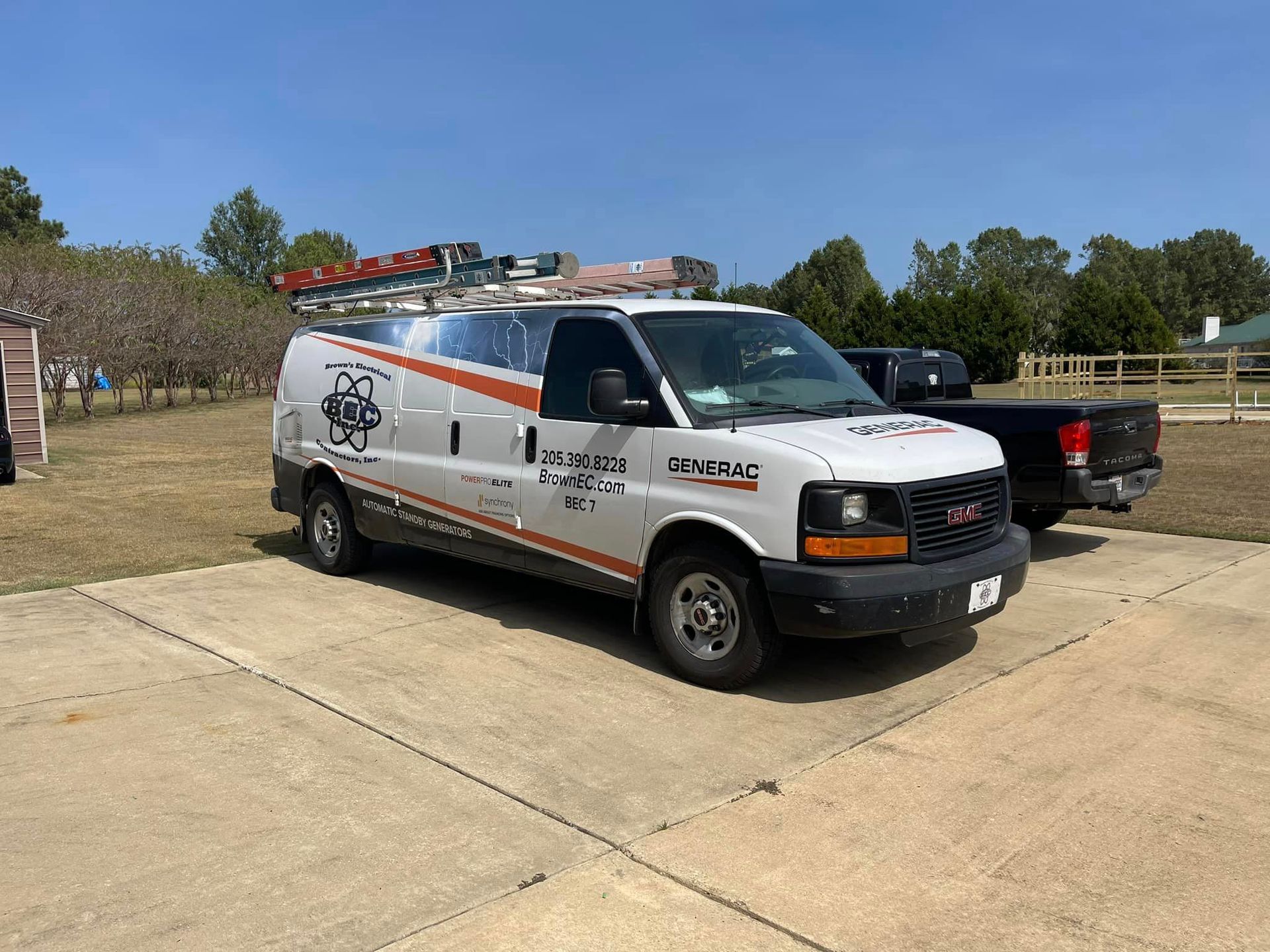 A white van is parked in a driveway next to a truck.