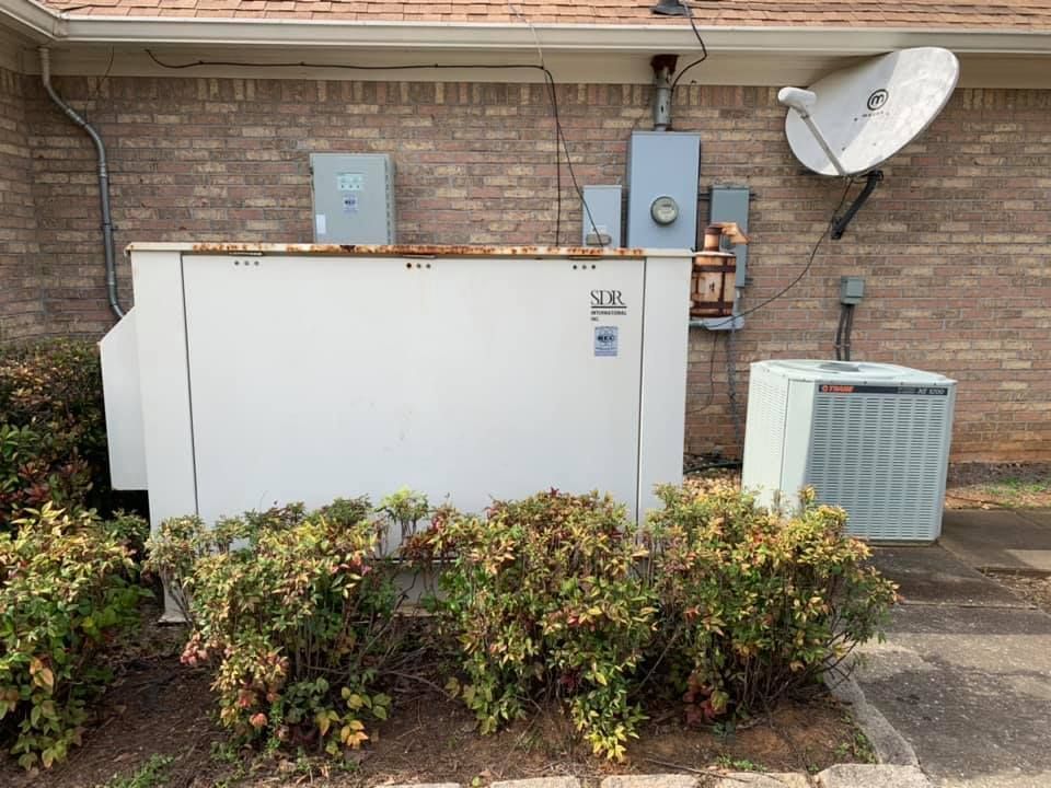 A white box is sitting on the side of a brick building next to a satellite dish.