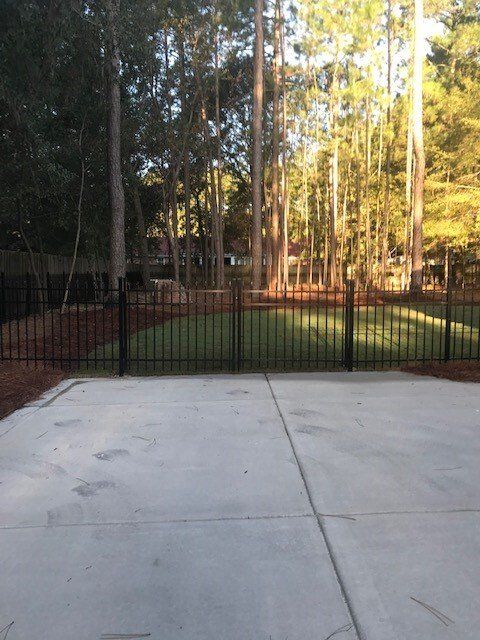 A concrete driveway with a fence and trees in the background