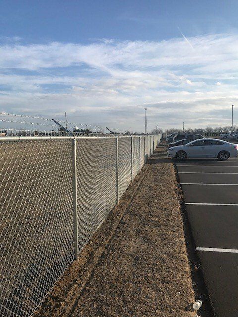 A chain link fence surrounds a parking lot with cars parked behind it.