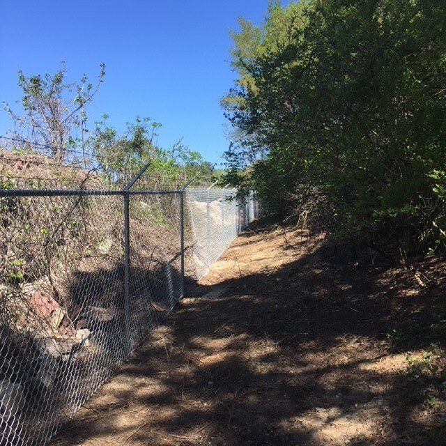 A chain link fence surrounds a dirt path in the woods.