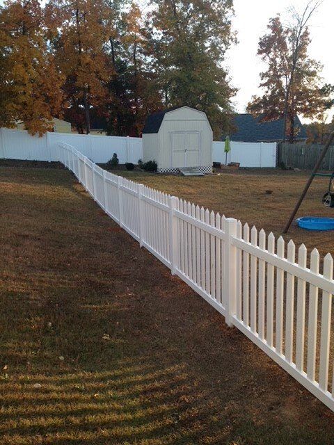 A white picket fence surrounds a backyard with a shed in the background
