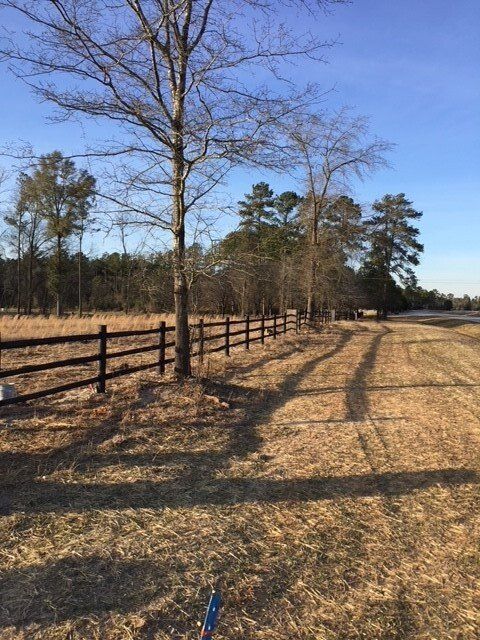 A wooden fence surrounds a dry grass field with trees in the background
