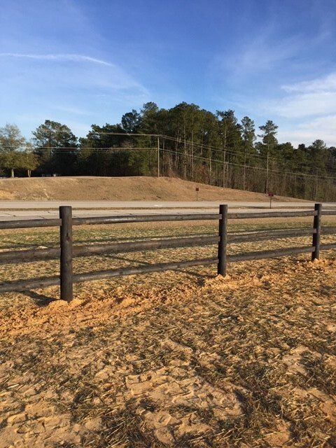 A wooden fence surrounds a dirt field with trees in the background.