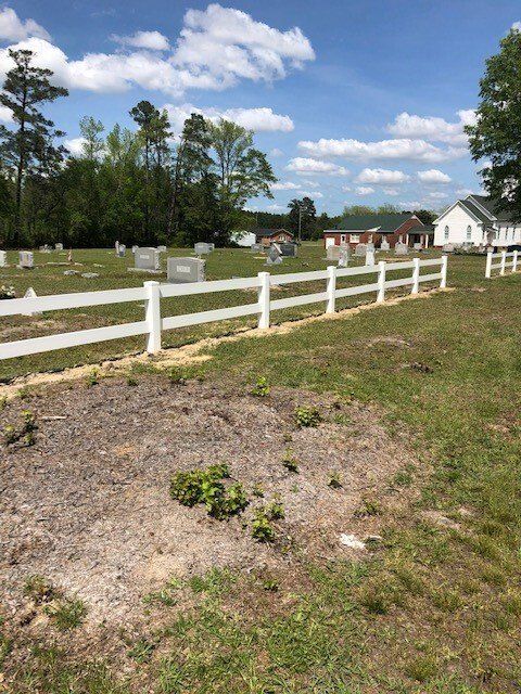 A white fence surrounds a cemetery on a sunny day