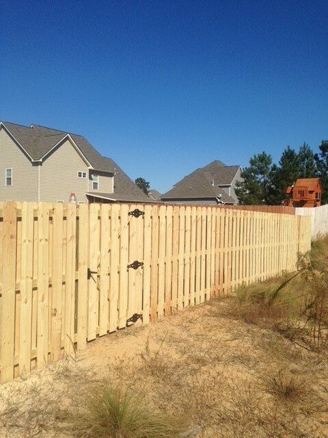 A wooden fence surrounds a dirt field in front of a house.