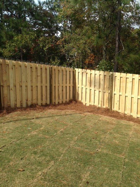 A wooden fence surrounds a lush green lawn in a backyard.