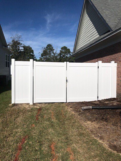 A white fence with a gate in the backyard of a house.