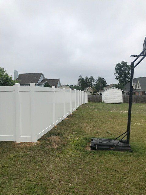 A white fence surrounds a basketball hoop in a backyard.