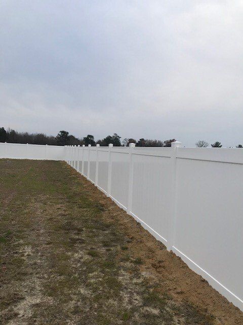 A long white fence surrounds a grassy field.