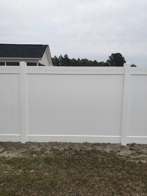 A white fence is sitting in the middle of a grassy field in front of a house.