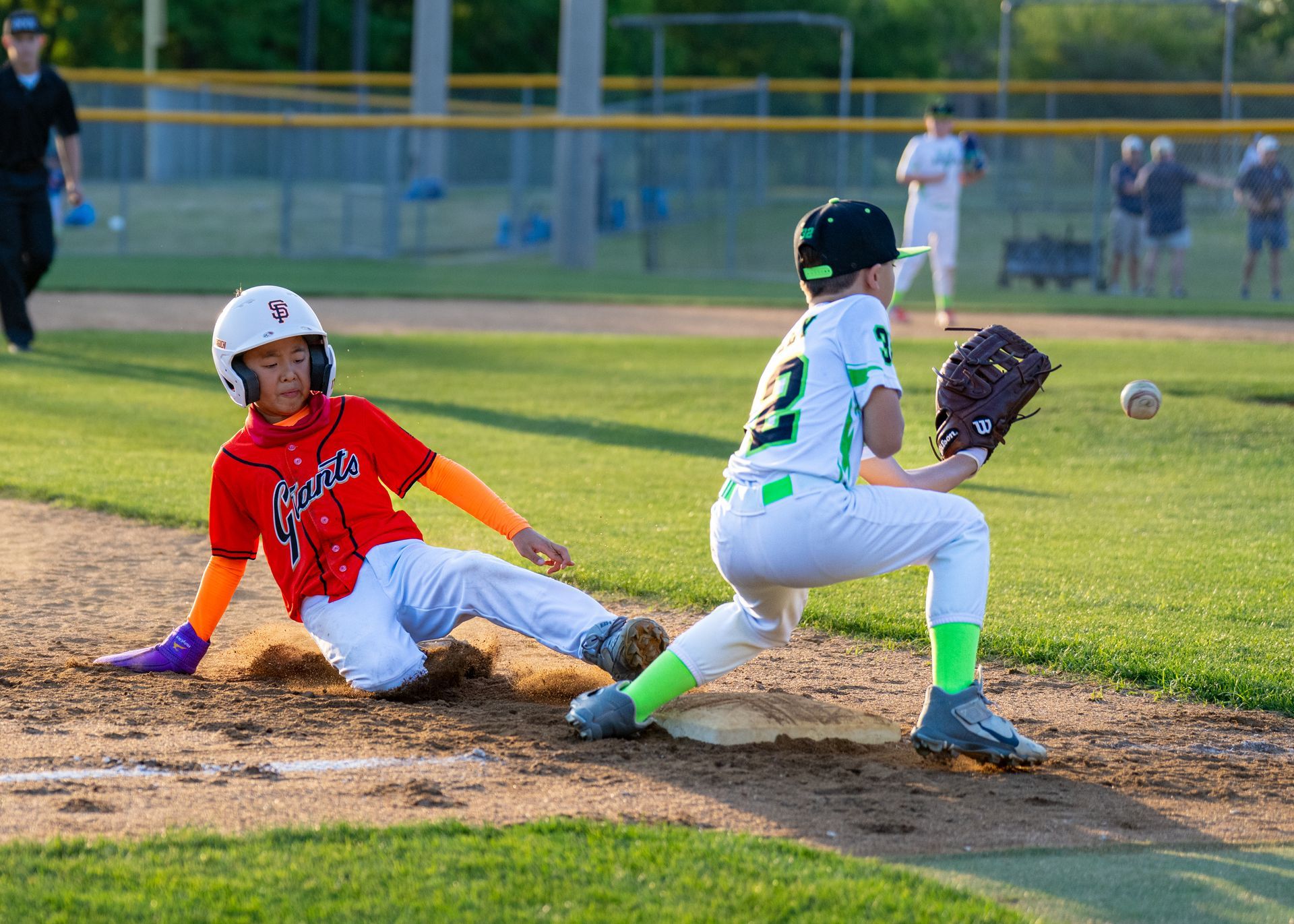 Youth baseball player in red slides into home as catcher in white tags the base.