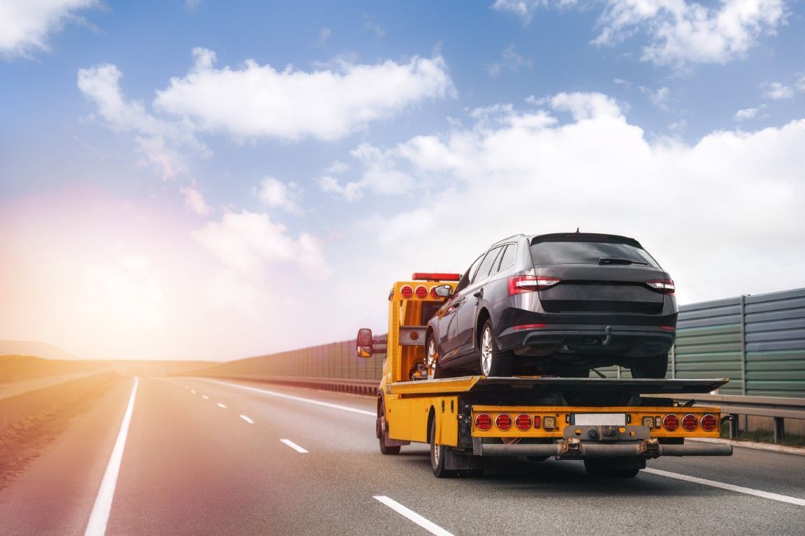 Tow truck transporting a black car on a sunny highway.