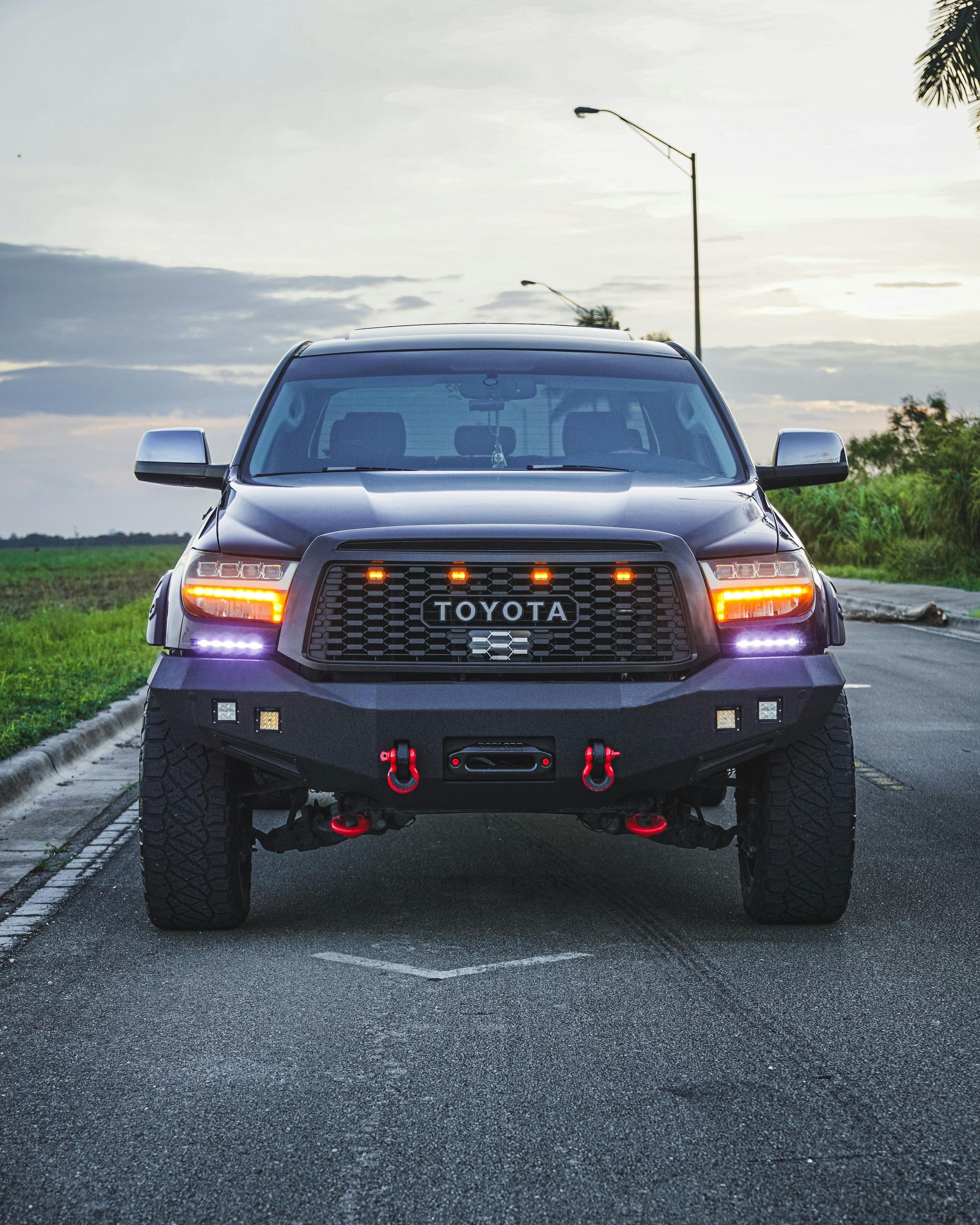 Black Toyota Tundra truck, modified with off-road bumper and lights, parked on a road at dusk.