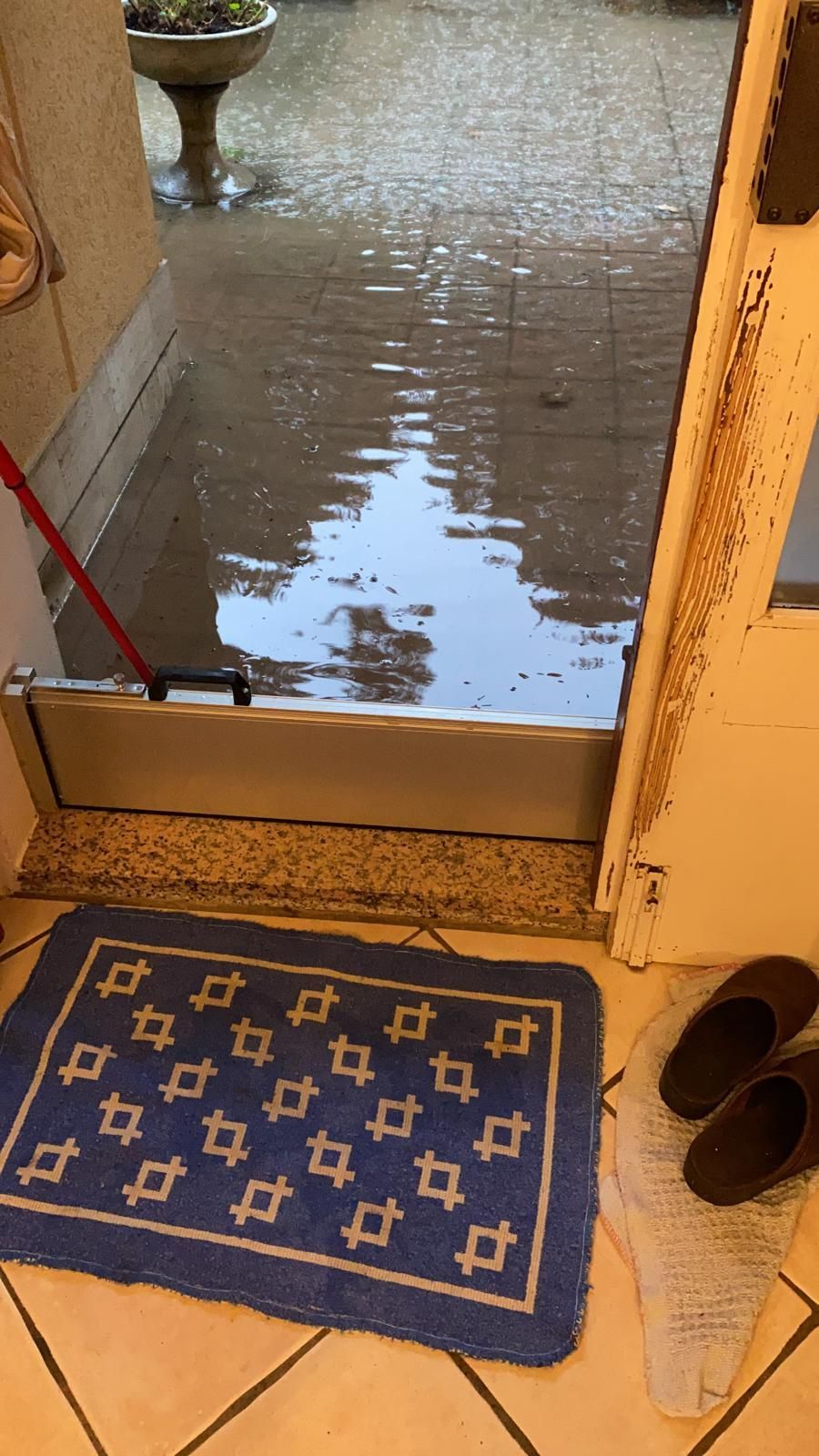 Una barriera antiallagamento installata sulla soglia di una porta per impedire all'acqua di entrare in casa, con un tappeto decorato e pantofole all'interno.