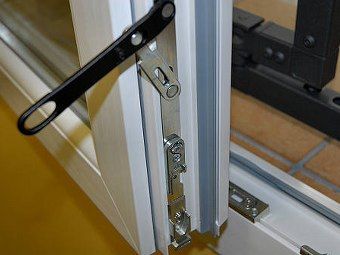 Vista ravvicinata di un telaio di finestra bianco con meccanismo di chiusura in metallo e braccio di supporto nero ad esso collegato.