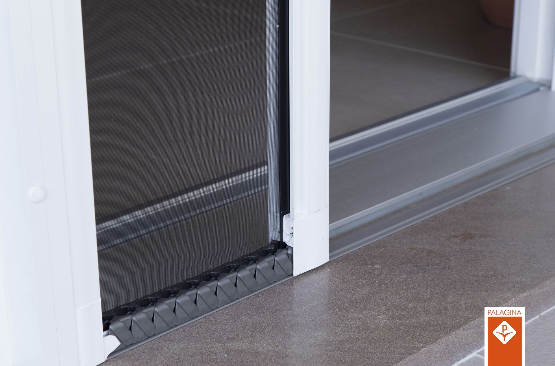 Una porta a zanzariera a scomparsa e plissettata, installata in un telaio bianco su un pavimento grigio.