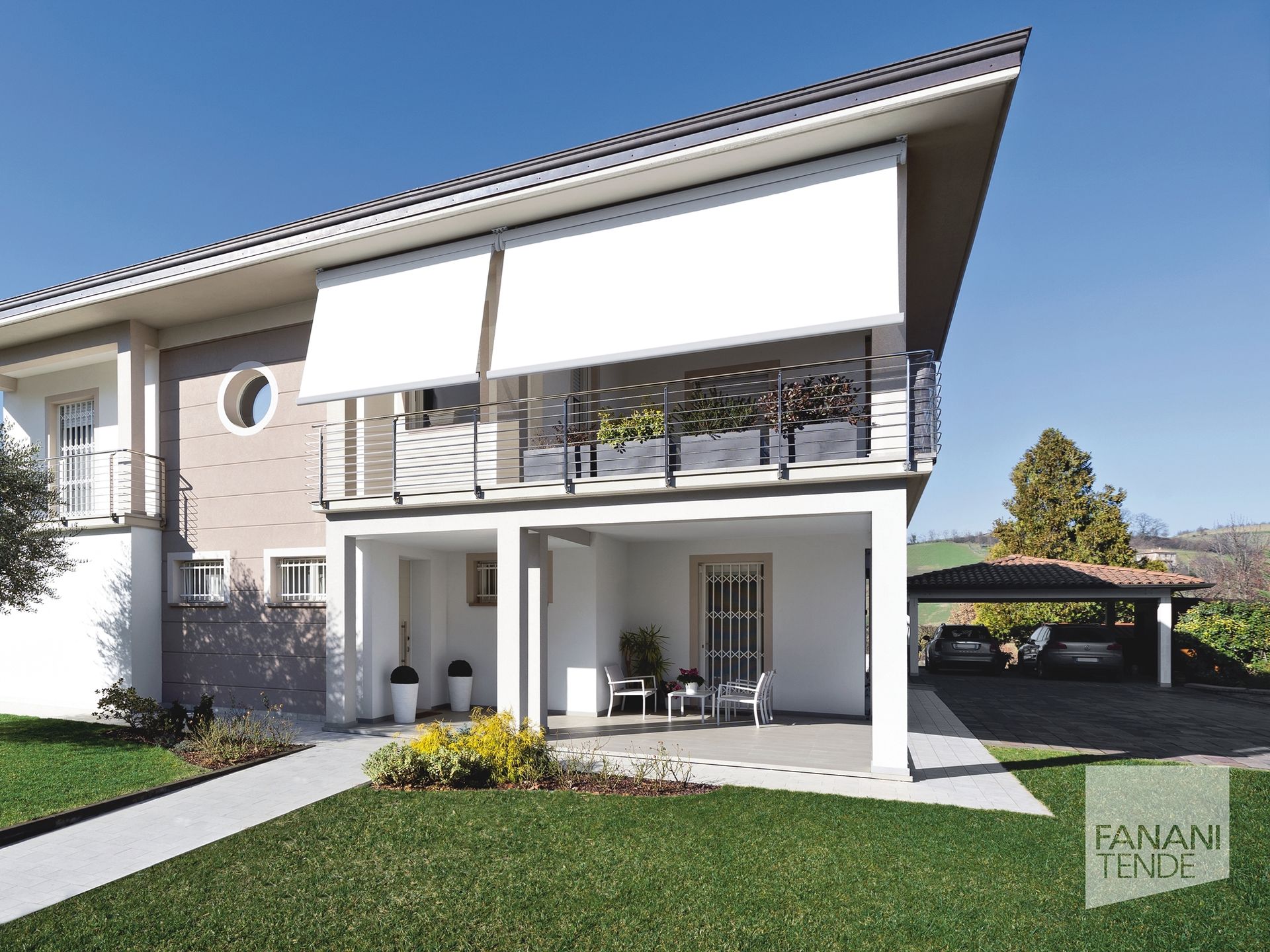 Esterno di una casa moderna con balcone ombreggiato, tende da sole bianche, patio al piano terra e posto auto coperto in un cortile erboso.