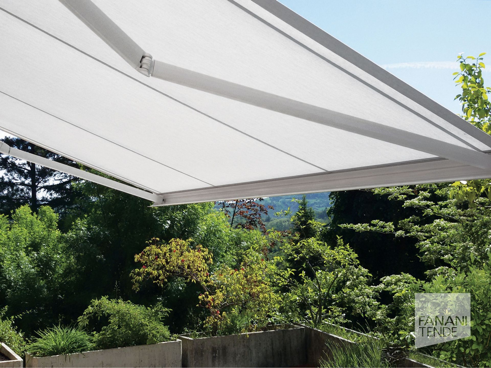Una tenda da sole bianca retrattile si estendeva su un balcone con alberi rigogliosi e un paesaggio visibile sullo sfondo.