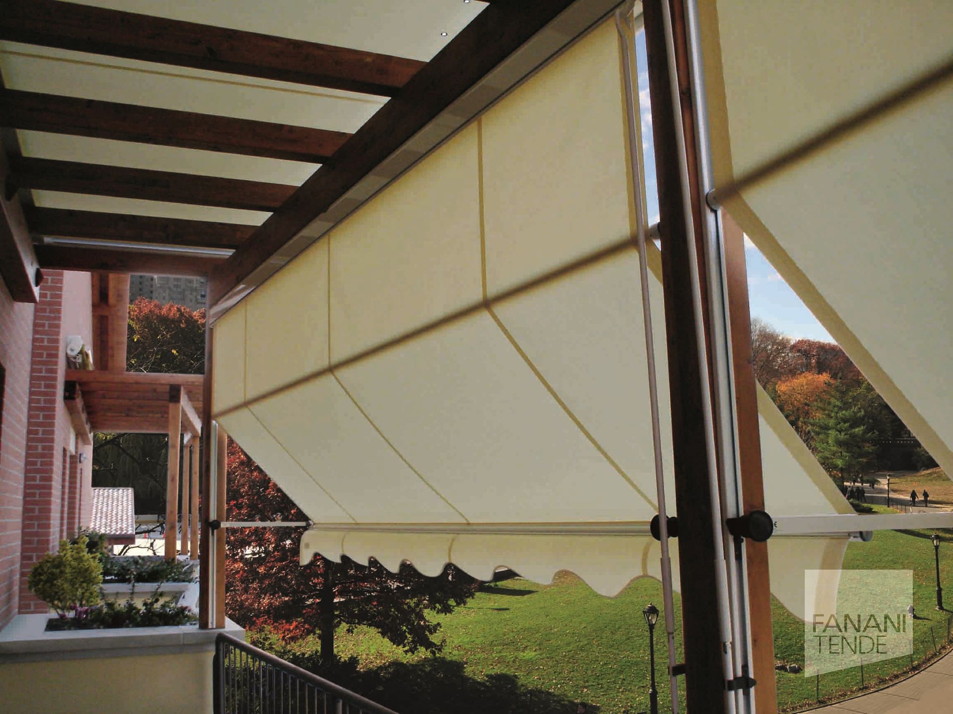 Tende da sole in tessuto color crema installate su un pergolato in legno, con vista su un prato.