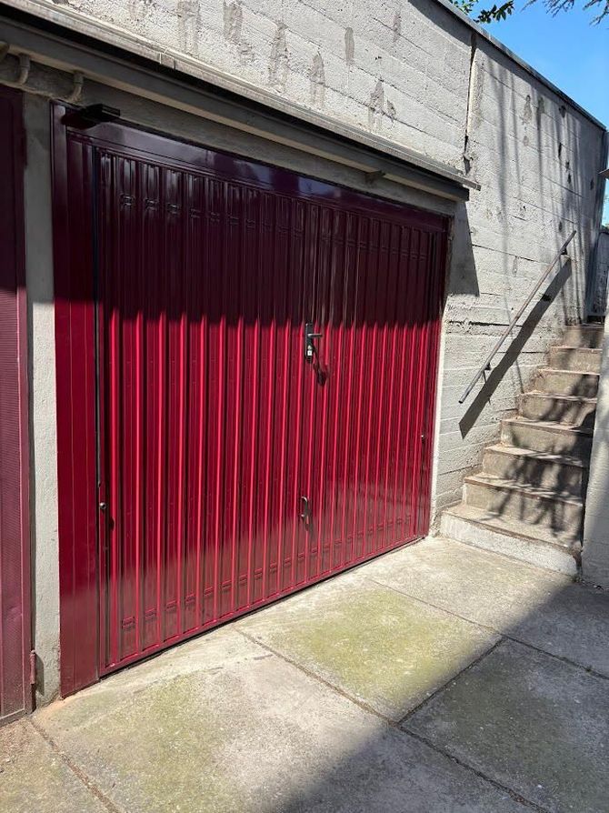 Un edificio ornato, color salmone, con finestre ad arco e un grande portone di legno, con persone che camminano per strada al di sotto.