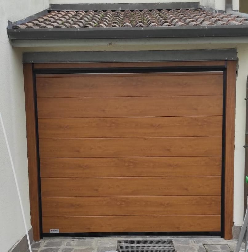 Una facciata color beige con due porte d'ingresso in legno scuro, pannelli laterali in vetro e una siepe ornamentale in vaso ai lati di ciascun ingresso.