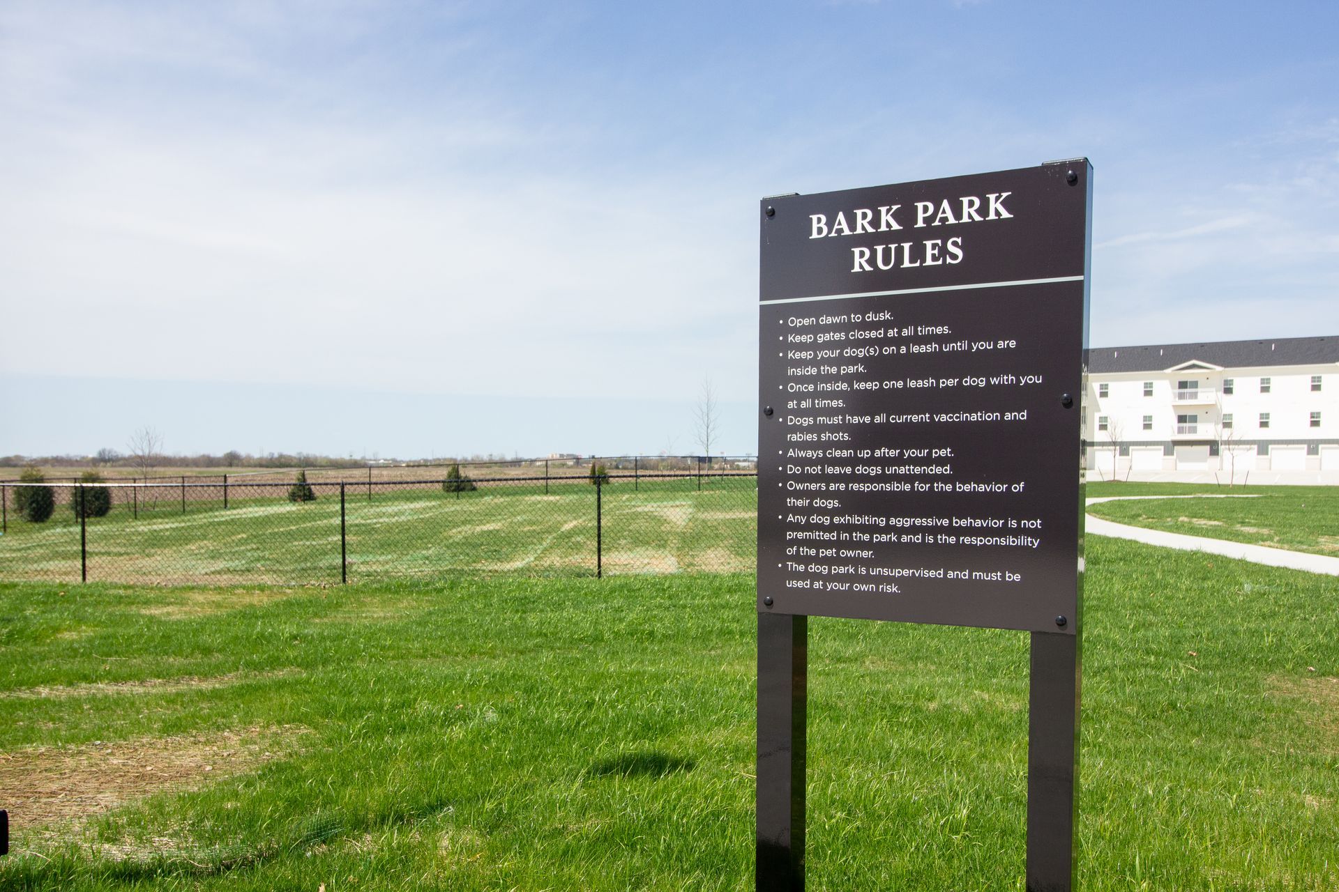 A sign in a grassy field says bark park rules