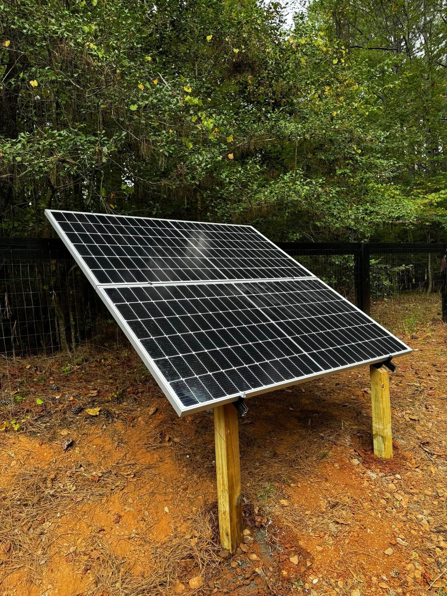 A solar panel is sitting on top of a wooden post in the dirt.