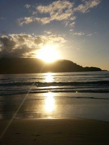 The sun is setting over the ocean with a mountain in the background