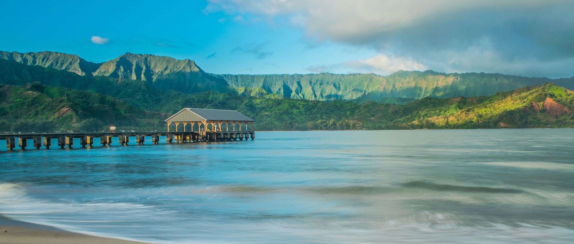 A pier in the middle of a body of water with mountains in the background.