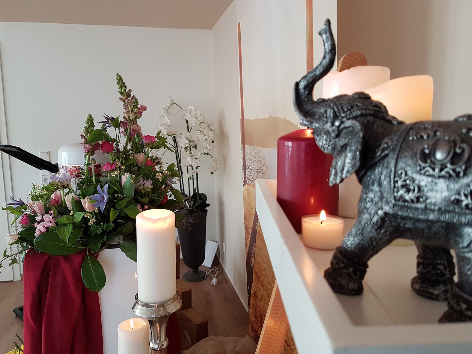 Eine Elefantenstatue sitzt auf einem Regal mit Kerzen und Blumen