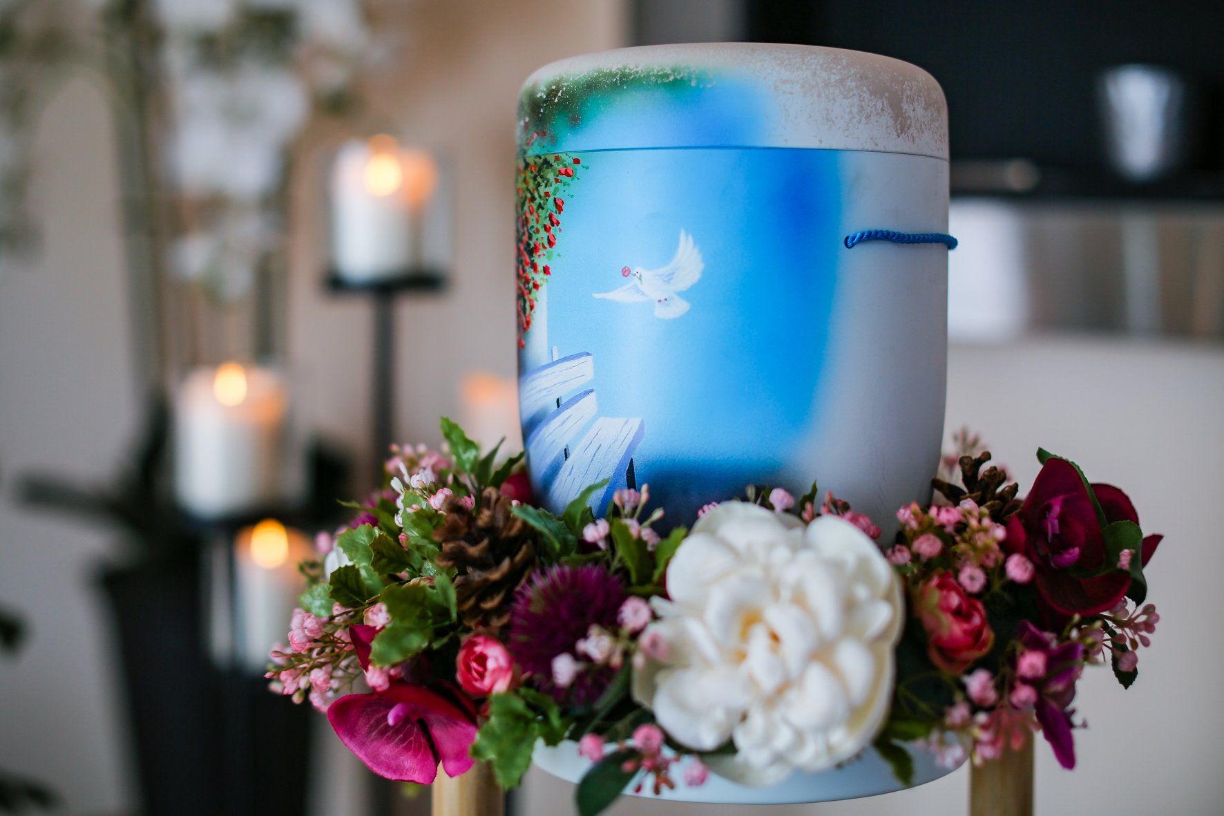 Eine blau-weiße Urne mit Blumen und Kerzen darum herum