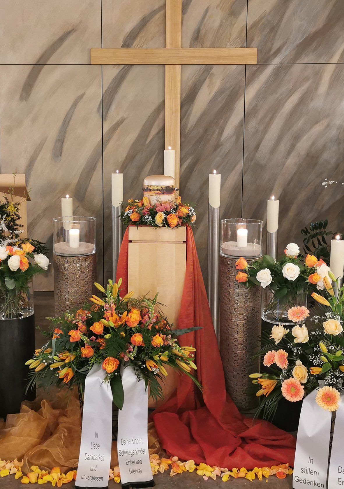 Ein Holzkreuz ist von Blumen und Kerzen umgeben