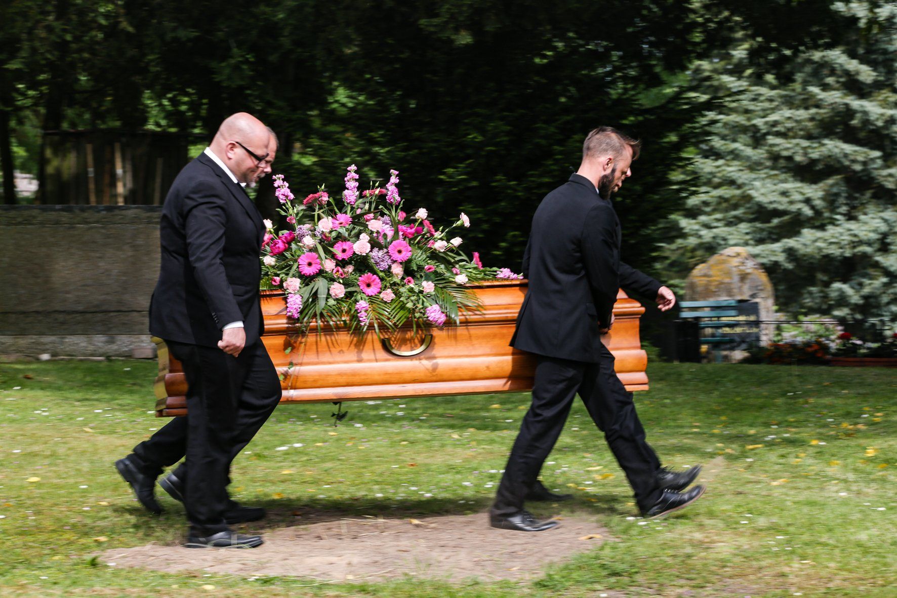 Zwei Männer tragen einen Sarg mit Blumen darauf