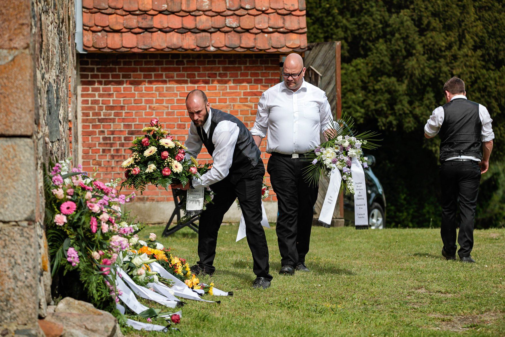 Zwei Männer legen Blumen vor einem Backsteingebäude nieder