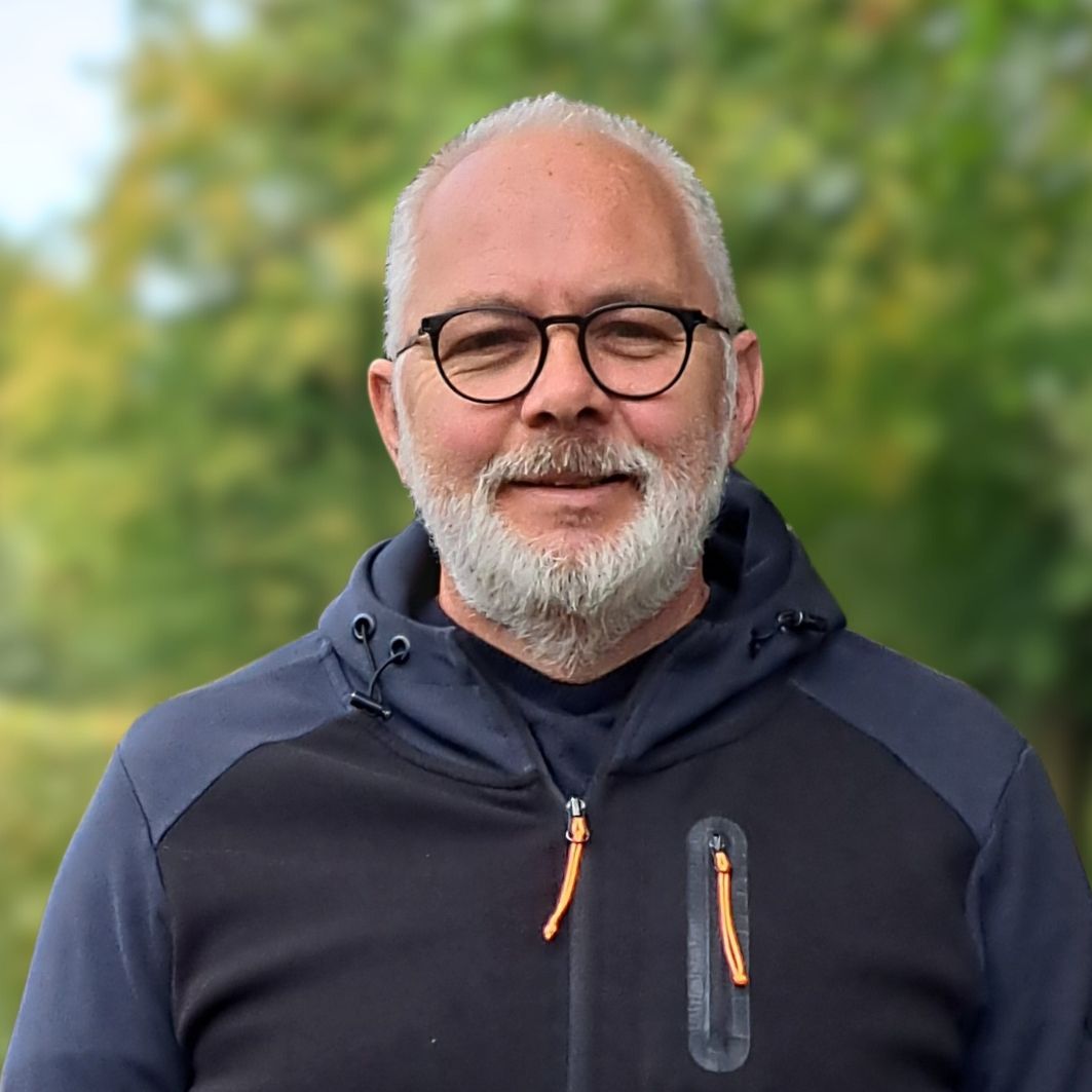 Ein Mann mit Bart und Brille trägt eine schwarze Jacke.