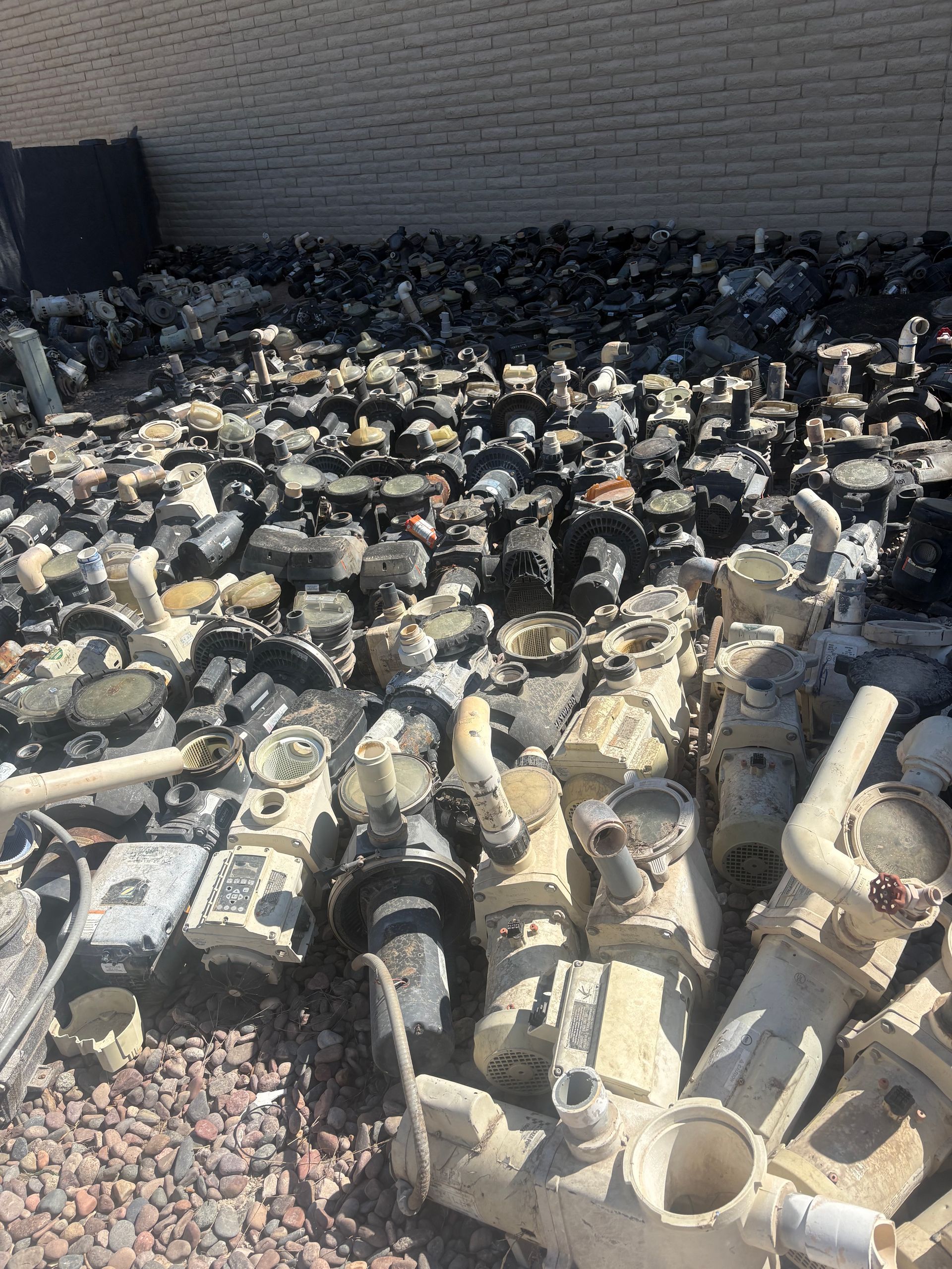 Pile of used water pumps in an outdoor lot, various colors and sizes.