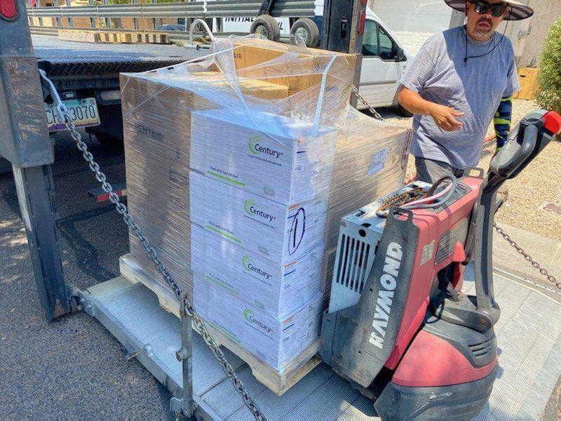 A man is pushing a raymond pallet truck with boxes on it.