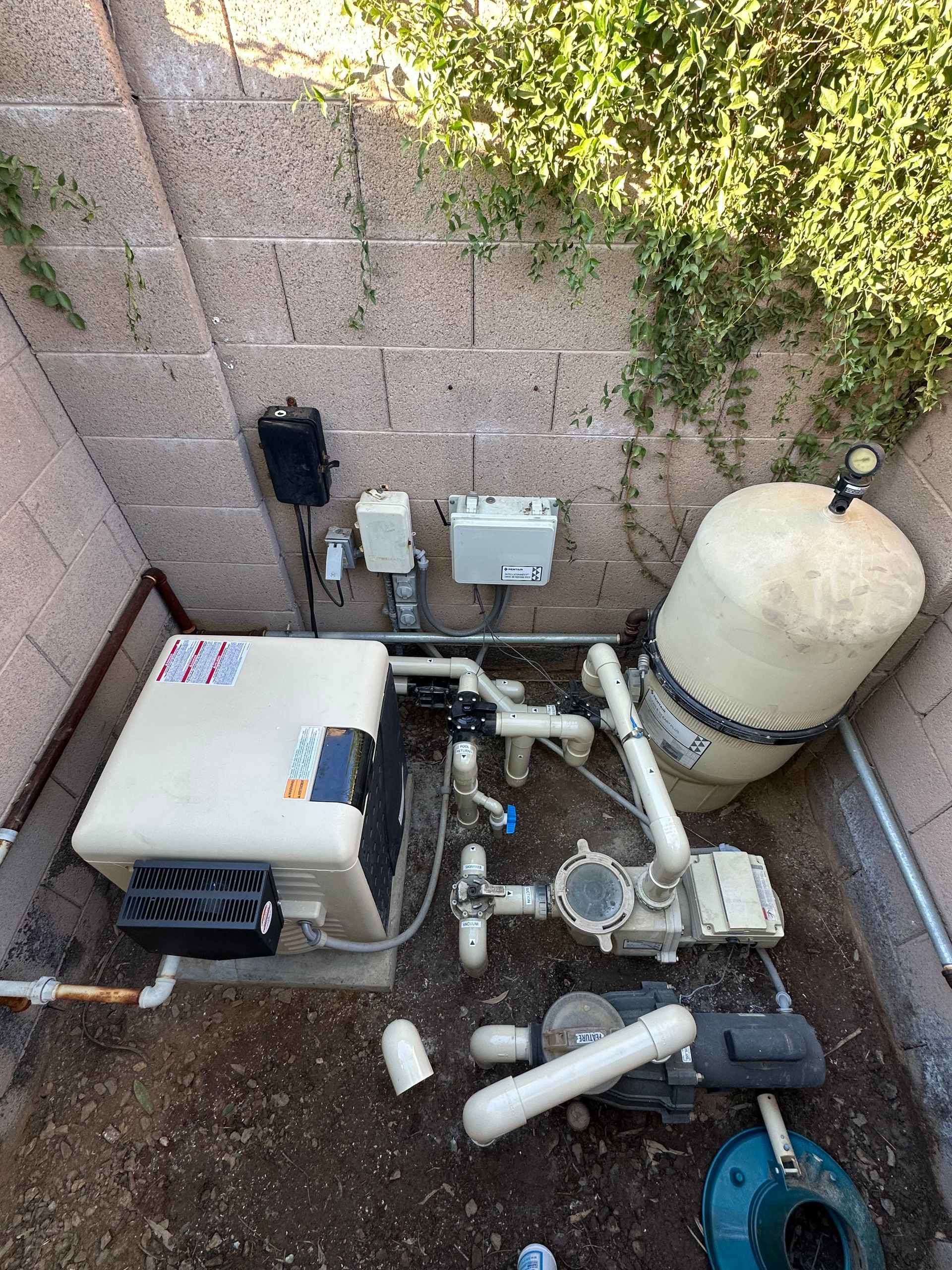 Pool equipment setup in a brick-walled enclosure, including a filter, pump, and heater.