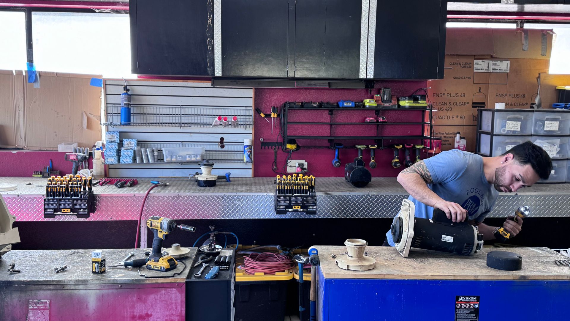 Mechanic working on a machine at a workbench in a workshop. Tools and parts are scattered around.