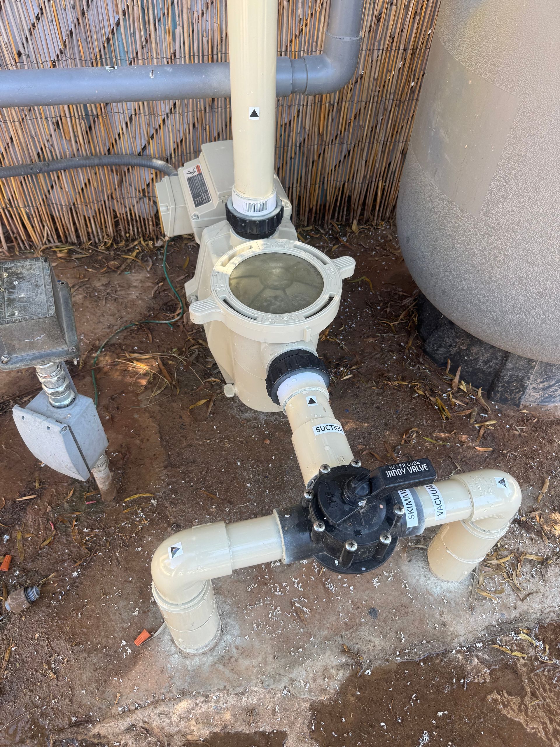 Pool pump and filter system with pipes and a multi-port valve, set on concrete next to a wall.