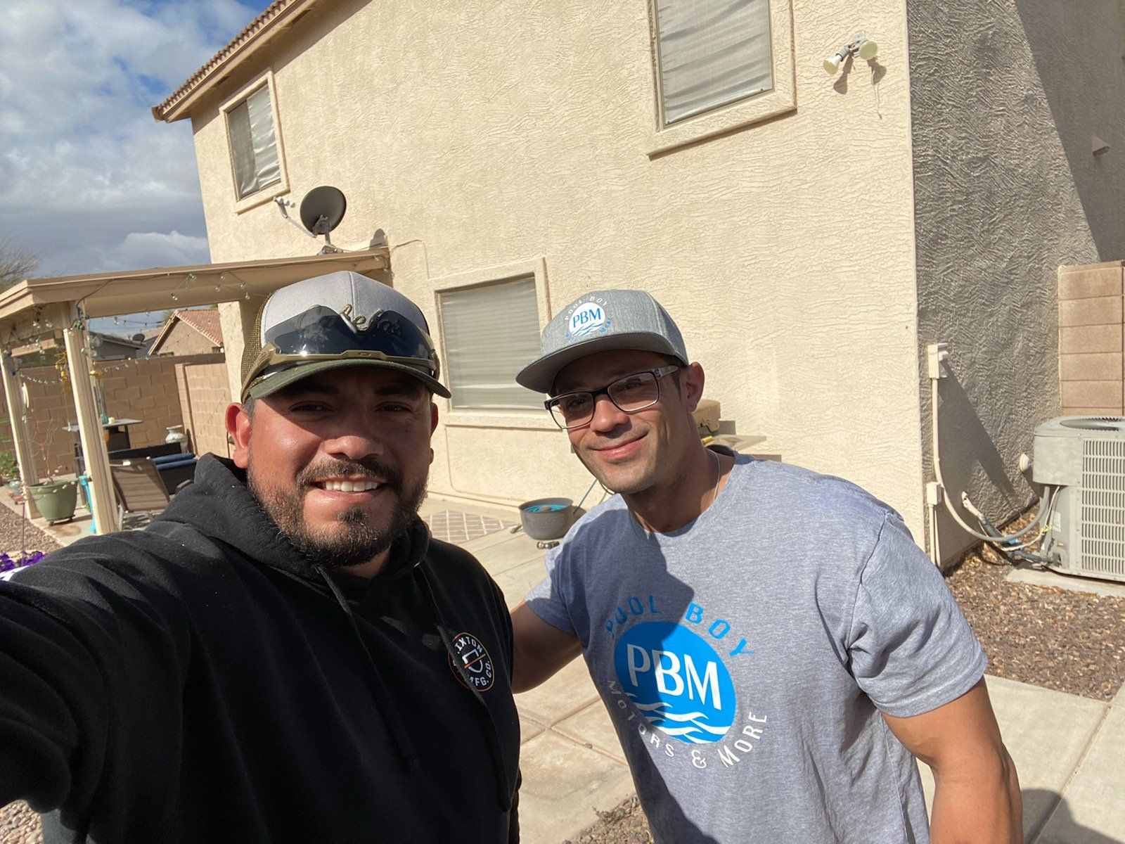 Two men are posing for a picture in front of a house.