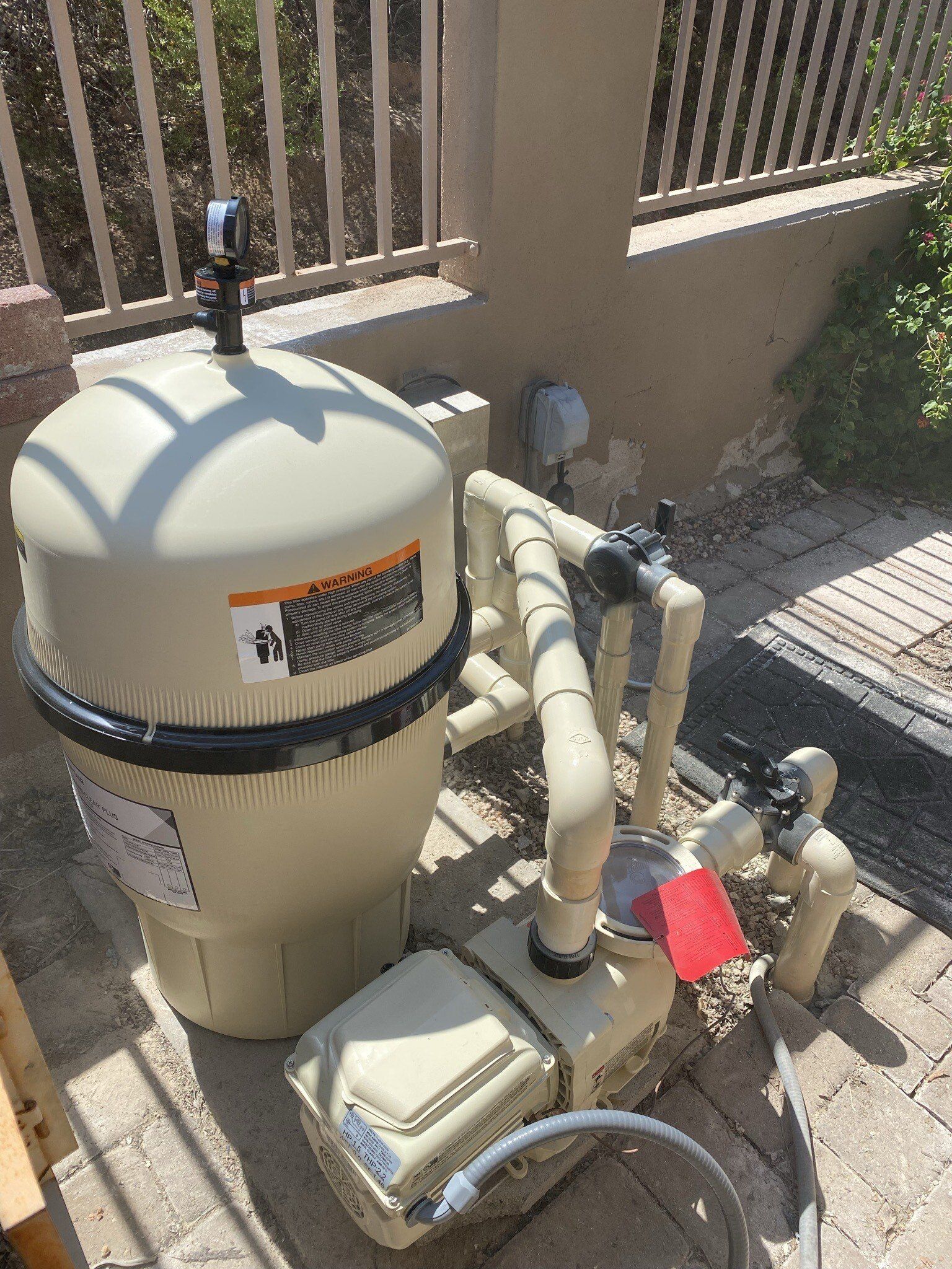 A swimming pool filter is sitting on the sidewalk next to a fence.