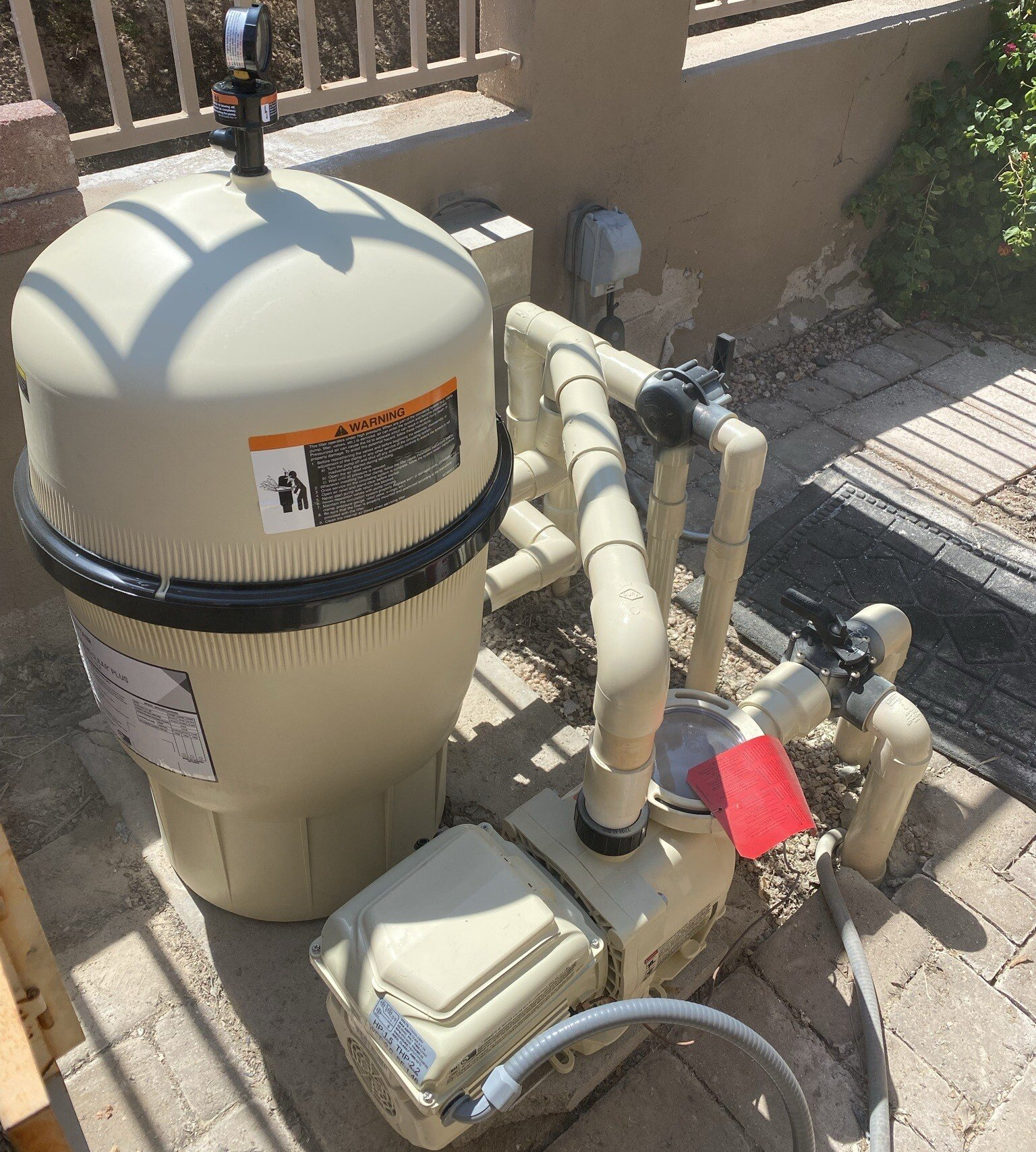 A swimming pool filter is sitting on the ground next to a hose.