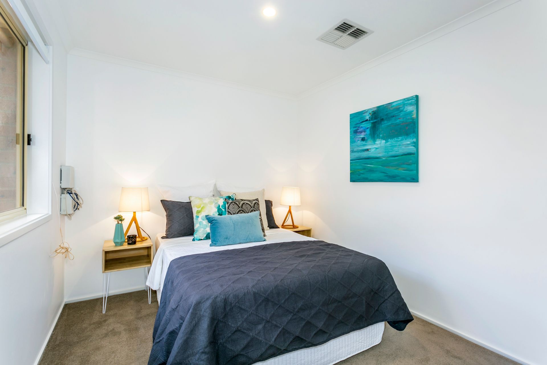 Bedroom with bed, bedside tables with lamps, window, and abstract blue artwork.