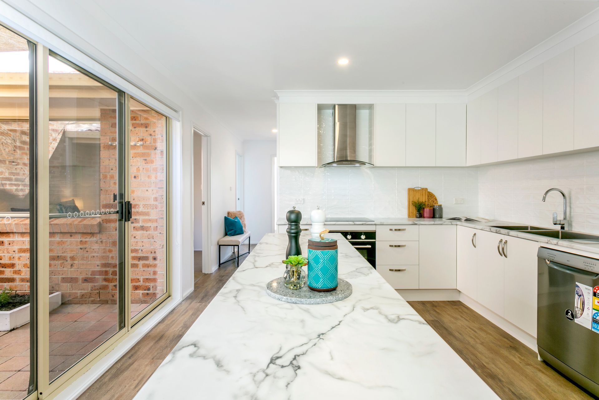 Modern kitchen with white cabinets, marble island, stainless steel appliances, and a glass door to a brick patio.